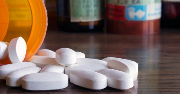 Photo of a medication bottle spilling white pills onto table top.