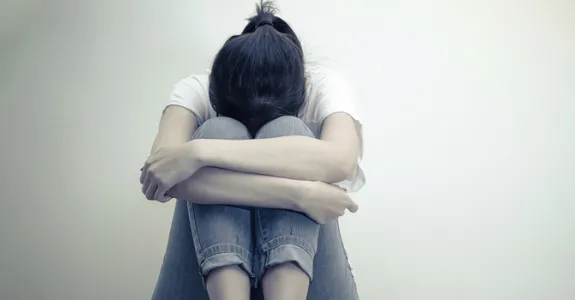 Photo of girl huddling against wall.
