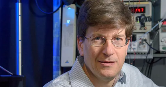 Photo of male PI in front of lab equipment.