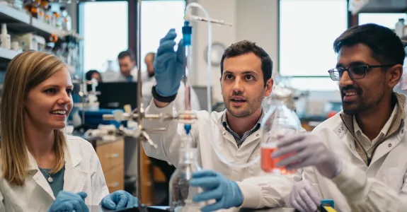 Photo of 3 graduate students at a lab bench, working with a piece of equipment.