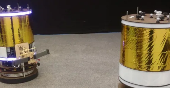 Photo of two of the space robots, which are large cylinders with gold foil around them and a ring of lights at the top.