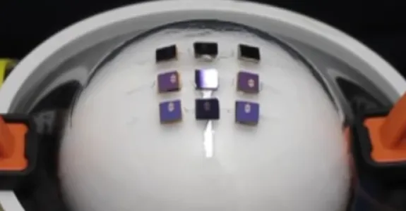 Screenshot image from video where test machine with orange clamps stretches translucent flexible electronic over a sphere.