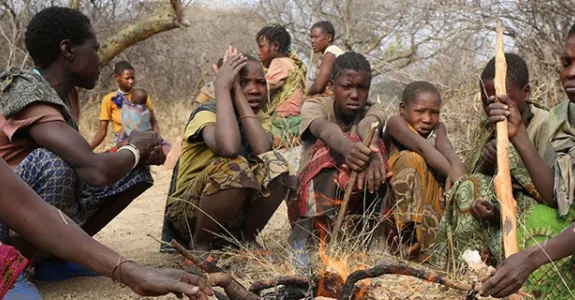 Photo of several members of the Hazda hunter-gatherer tribe in Tanzania crouched around a fire.