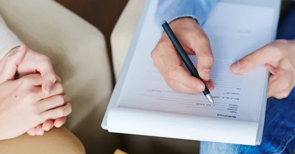 Photo of patient and therapist's hands during a meeting, therapist writing on a clipboard.