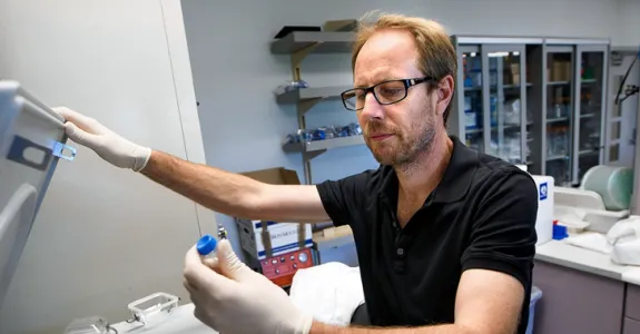Photo of Dr. Tony Wyss-Coray examining a small test tube sample taken out from a centrifuge in the laboratory.