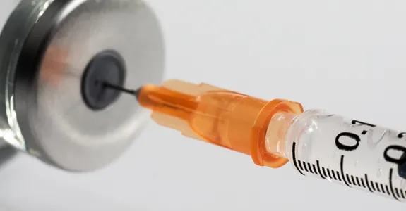 Photo of a needle going into a vaccine container.