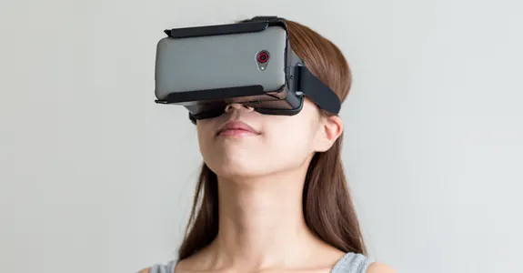 Photo of a woman wearing a virtual reality headset in front of a gray background.