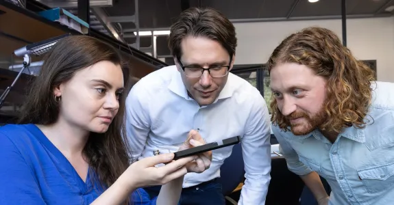 Photo of faculty member and two researchers looking at a device in the lab.