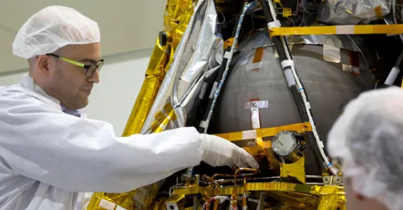 Photo of Stanford Bio-X Fellow graduate student Yonatan Winetraub inserting an object into a spacecraft, wearing protective clothing.