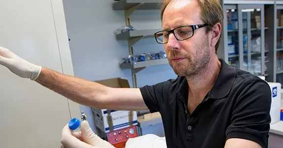 Photo of Dr. Tony Wyss Coray lifting a vial out of a piece of equipment in the laboratory.