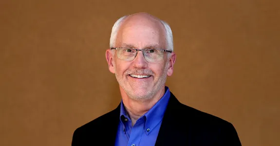 Photo of Dr. Paul Yock standing in front of a brown background.
