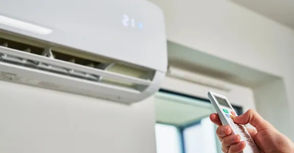 Photo of a person's hand holding a remote up towards a ventilation system.