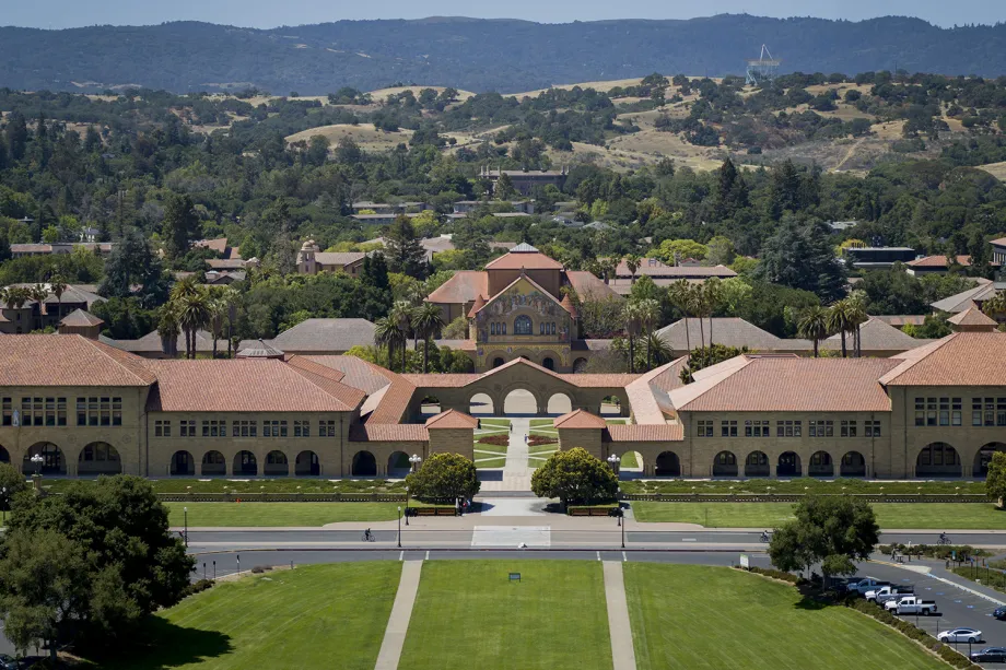 Outdoor overhead photo of Stanford campus, focused on the entrance to the main quad with the Memorial Church facade visible, with the foothills in the background.