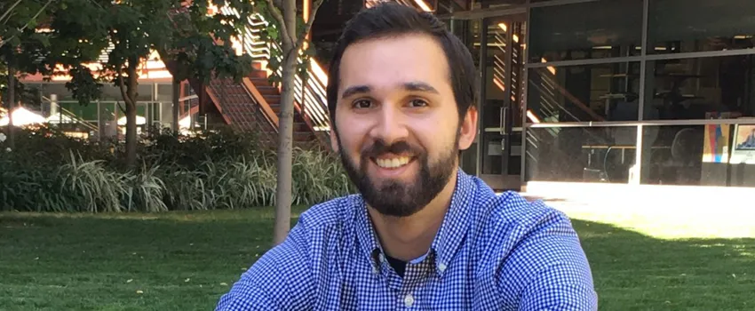 Photo of bearded young man sitting on the lawn at the James H. Clark Center.