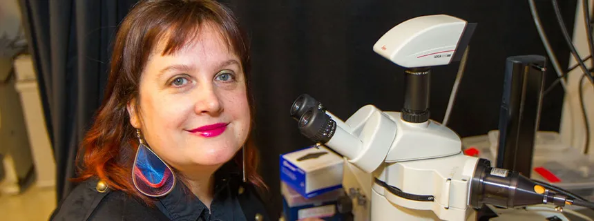 Photo of Dr. Maria Barna in the lab next to a microscope.