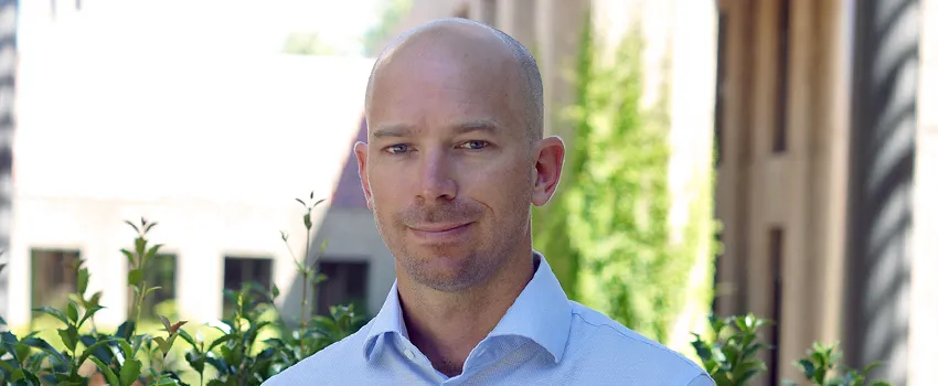Photo of Dr. Ben Domingue in front of trees and a building.