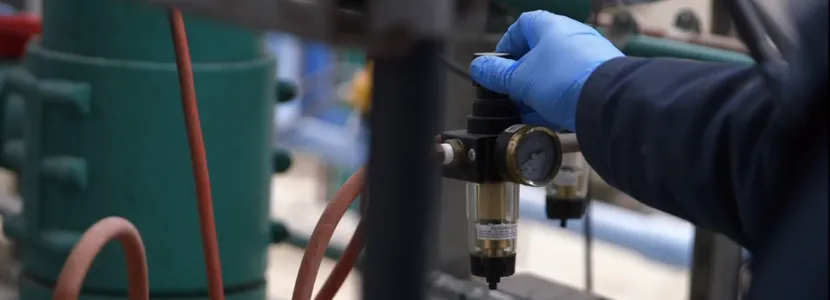Screenshot/image of a man's hand in a blue glove adjusting a valve on a pipe.