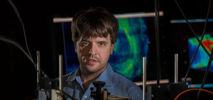 Photo of Dr. Karl Deisseroth in the laboatory, with colorful brain scans in the background.