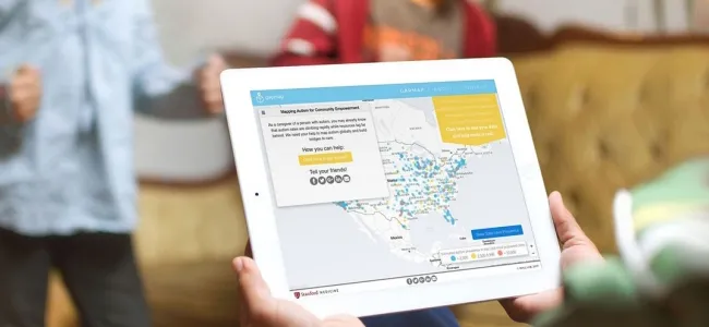 Photo of person holding iPad, with screen displaying GapMap tool, while two children play in the background.