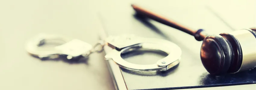 Photo of a gavel on top of a law book with a pair of handcuffs beside it.