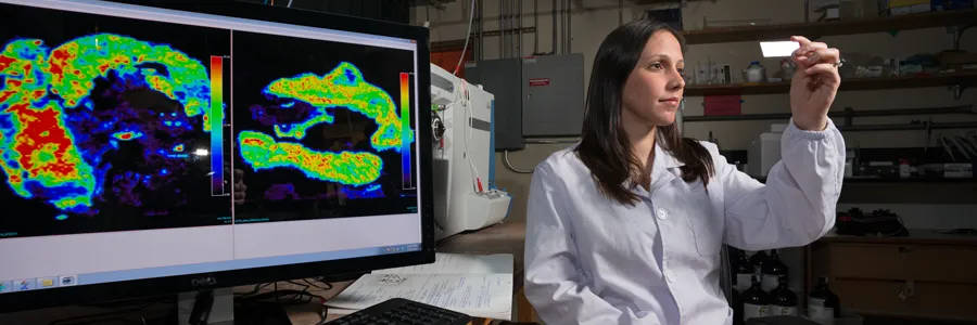 Photo by L.A. Cicero of Livia Eberlin, a postdoctoral scholar in chemistry, examines a stained sample against a backdrop of images from gastric cancer surgery and the mass spectrometer she uses in her interdisciplinary research.