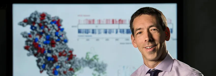 Photo of Dr. Euan Ashley in front of a screen showing a 3D image of a molecule.