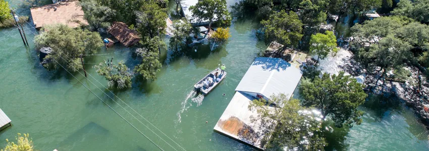 Photo showing a small motorboat with a few people inside moving around houses and trees almost entirely submerged by flooding.