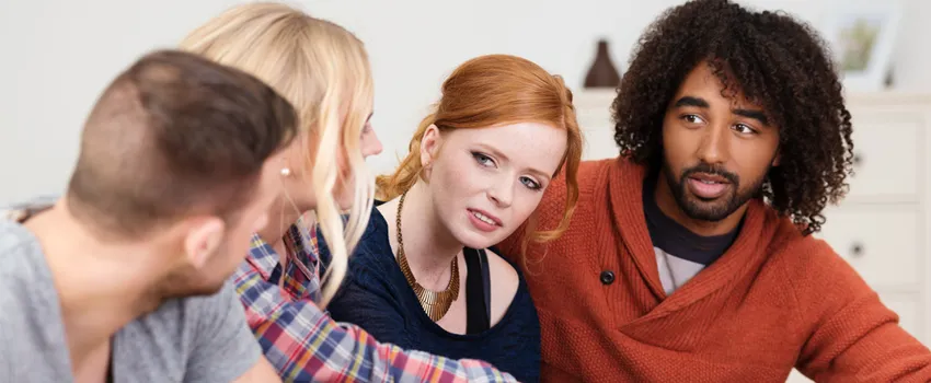 Photo of four diverse young people sitting together in a bedroom.