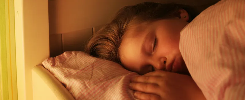 Photo of little girl sleeping in a bed with her hand beside her pillow.
