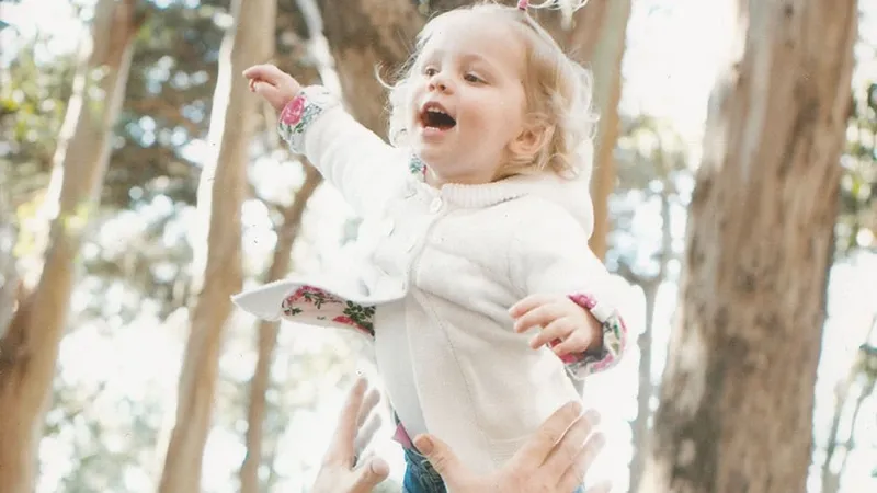 Photo of a man tossing his blonde toddler daughter in the air.