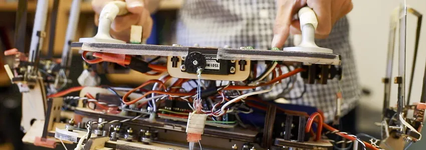 Student lifting up the robotic gripper by two handles, showing its interior wires.