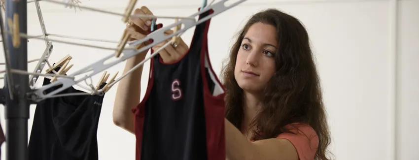 Photo of undergraduate girl hanging Stanford-logo running tops on a rack with clothespins.