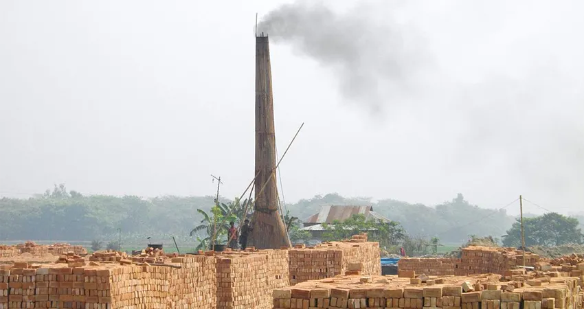 Photo of a tall kiln tower streaming smoke with many huge stacks of orange/red bricks in front of it.