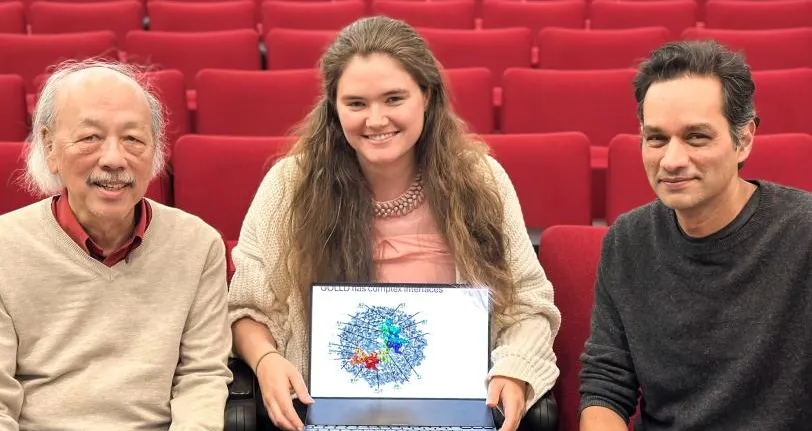 Photo of Professor Wah Chiu, graduate student Rachael Kretsch holding a laptop showing a colorful structure on the screen, and Professor Rhiju Das, all seated indoors and smiling at the camera.