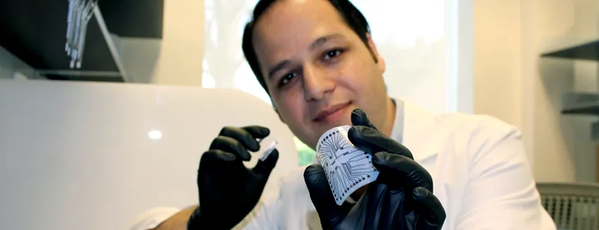 Photo of engineering research associate Rahim Esfandyarpour holding up and flexing small lab on chip device.