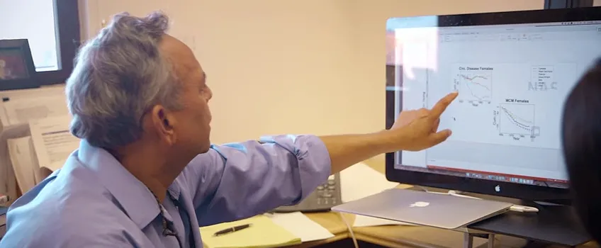 Screenshot of Dr. Shripad Tuljapurkar indicating graphs on computer screen.