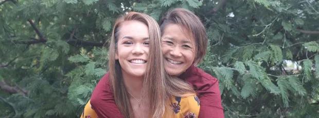 Photo of an Asian woman with her arms wrapped around her daughter from behind.