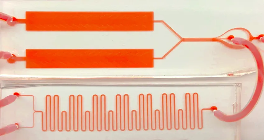 Photo depicting the device described in the article, showing two orange rectangles at the top, connected by orange wires and tubes to a microfluidic segment that looks like a tight wavy line.