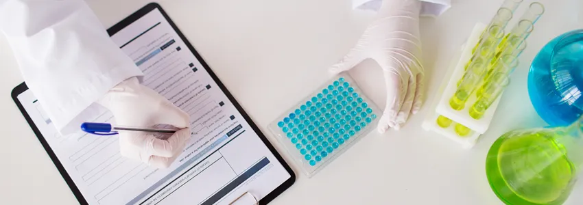 Photo of scientist taking notes on clipboard next to test tubes.