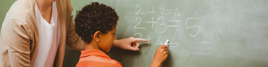 Photo of child doing math problems at chalkboard.