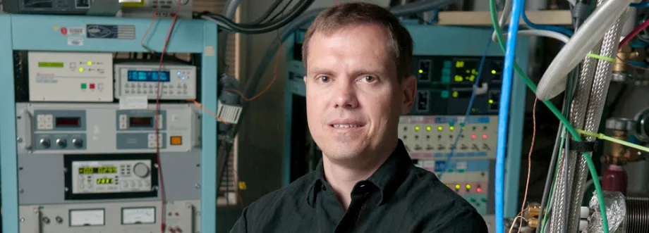 Photo of Dr. Nicholas Melosh in front of large pieces of equipment and several large wires.