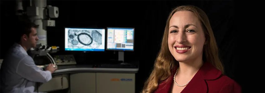 Photo of female PI in laboratory with cell images on screens in background.