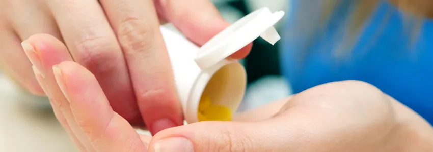 Photo of a woman's hands, pouring pills out of a bottle.