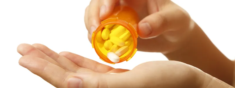 Photo of woman's hands pouring white pills out of a medication bottle into her palm.