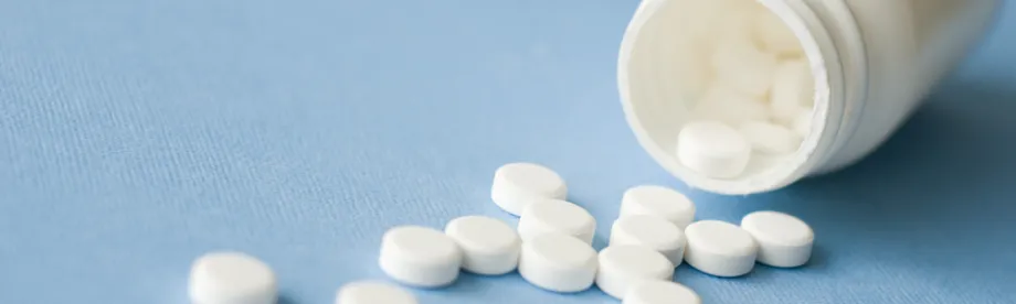 Photo of white bottle spilling white pills across a blue surface.