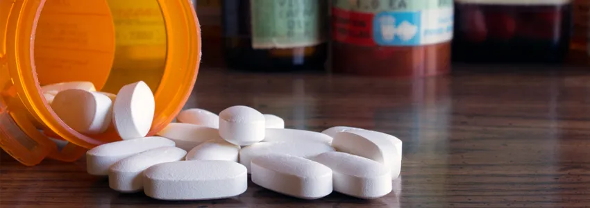 Photo of a medication bottle spilling white pills onto table top.