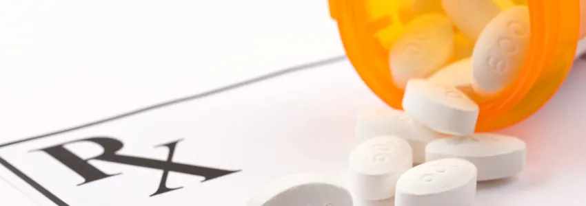 Photo of an orange medication bottle spilling white pills onto a scrip reading "RX".