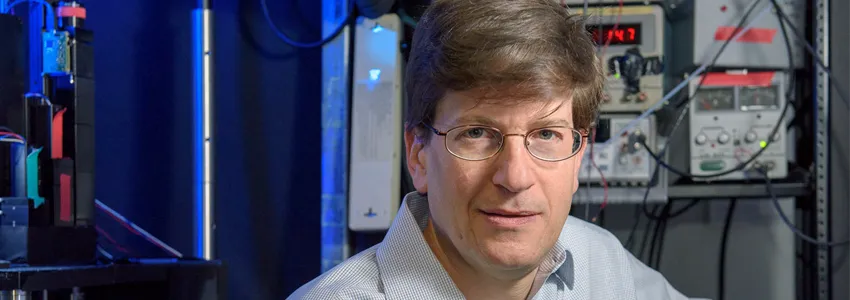 Photo of male PI in front of lab equipment.