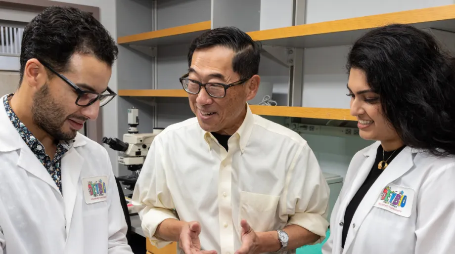 Indoor photo of Stephan Ramos, Professor Seung Kim, and Preksha Bhagchandani in the lab.