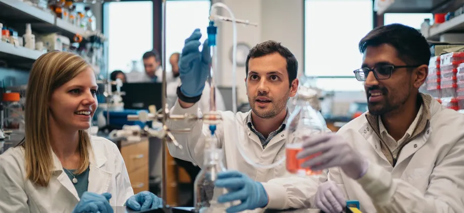 Photo of 3 graduate students at a lab bench, working with a piece of equipment.